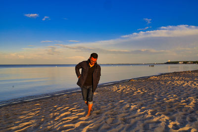 Rear view of man on beach against sky during sunset