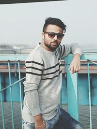 Portrait of young man standing by railing