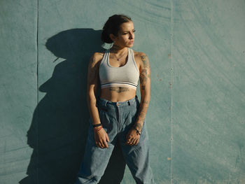 Young woman looking away while standing against wall