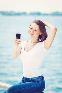 Young woman taking selfie with mobile phone against sea