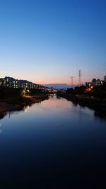 Illuminated city by river against clear sky at dusk