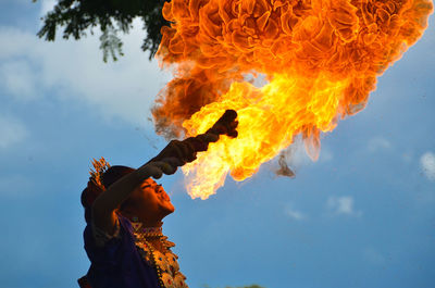 Low angle view of woman performing with fire against sky