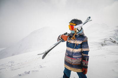 Portrait of a pretty and active woman skier, wearing a mask and holding skis in her hands, active