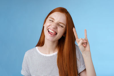Young woman making horn sign against blue background