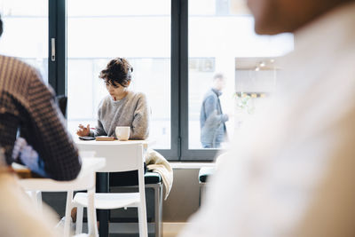 Female customer using mobile phone while sitting with coffee cup at table in cafe