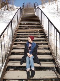 Full length of young woman sitting on steps during winter