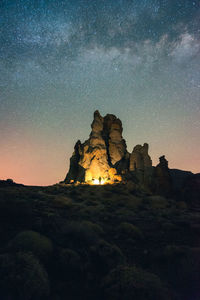 Low angle of explorer standing near rock with luminous flashlight under sky with glowing stars in long exposure in tenerife