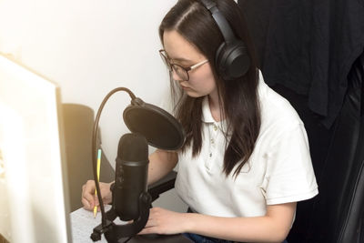 Woman with headphones taking notes and preparing for podcast recording in front of microphone