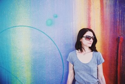 Young woman in sunglasses standing against wall