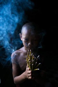 Portrait of shirtless boy holding incense while standing against black background