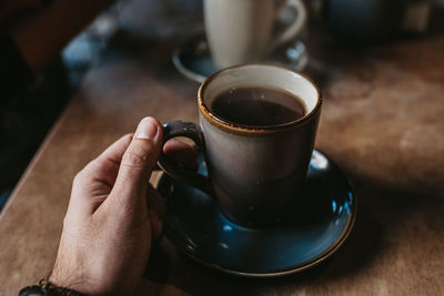 Crop hands of unrecognizable female sitting at wooden table holding hot coffee in a rustic mug