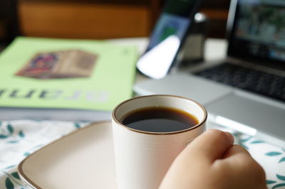 Cropped hand of woman holding coffee cup at table