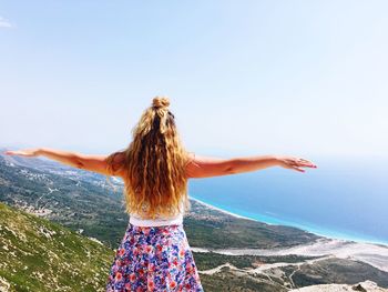 Rear view of woman with arms outstretched standing against clear sky