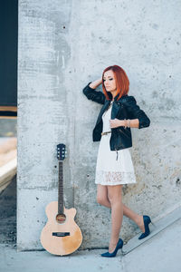 Full length of woman with guitar against wall