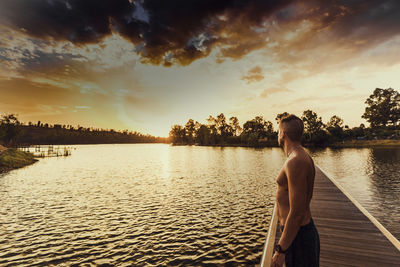 Side view of shirtless man standing on pier over during sunset
