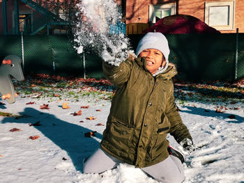 Portrait of smiling boy throwing snow during winter