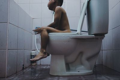 Full length of shirtless man sitting in bathroom