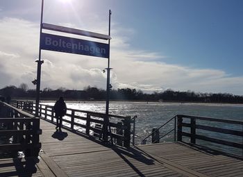 Woman standing on pier by lake against sky