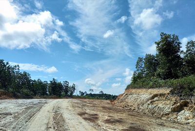 Dirt road by trees against sky