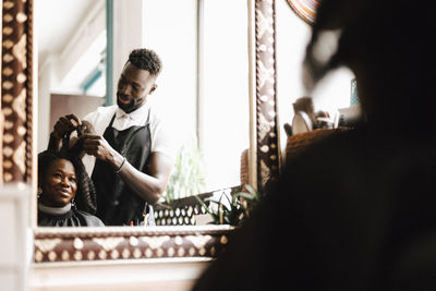 Male hairdresser making locs of female customer at barber shop