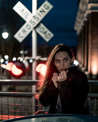 Thoughtful woman sitting at table against railroad crossing sign at night