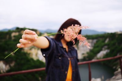 Woman showing flowers while standing against mountains