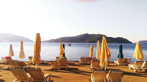 Deck chairs with parasols at beach against clear sky