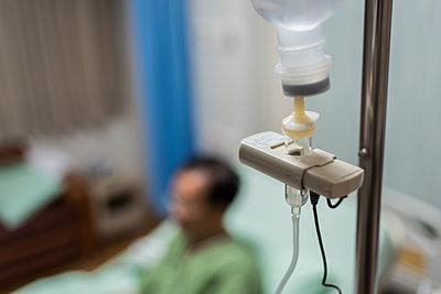 Close-up of iv drip with man on bed in hospital