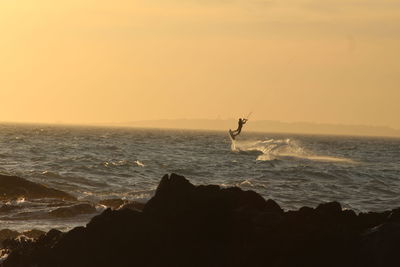 Silhouette man kiteboarding in sea against sky