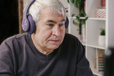 Cheerful older person with headphones working on computer. gray hair old man using laptop, watching