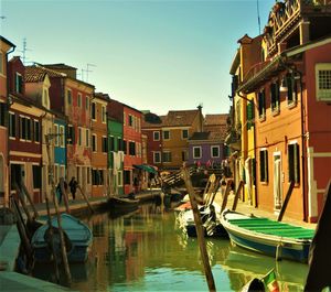 Boats moored in canal by buildings against clear sky