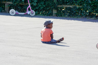 Boy wearing cap while sitting on road during sunny day