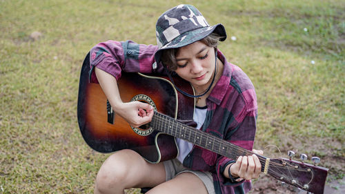 Woman playing guitar while sitting on grassy land