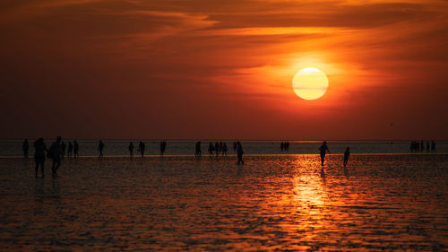 Silhouette people on beach against orange sky