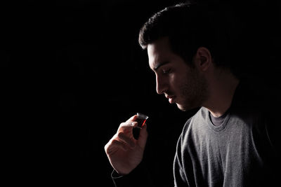 Side view of young man looking away against black background