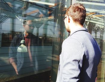 Young man standing by store window during sunny day