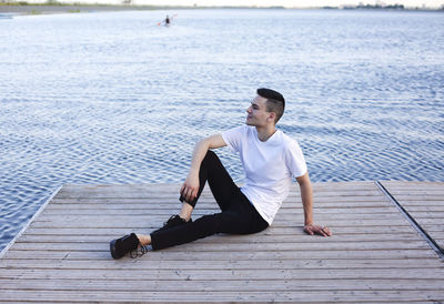 Young man sitting on pier over sea