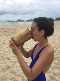 Side view of woman in swimwear having drink while standing at beach