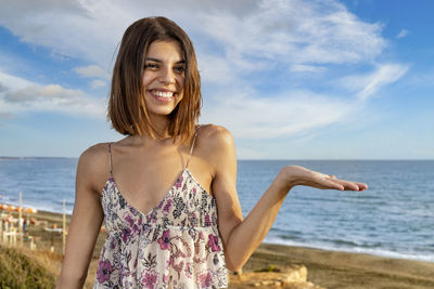 Smiling girl raising up her left hand to show a potential copy space on the right. 