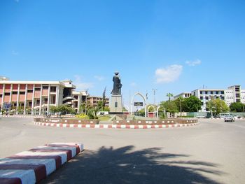 Statue on footpath in city against blue sky