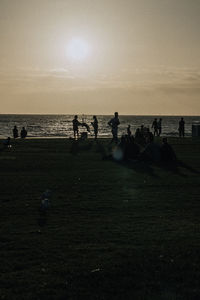 Silhouette people on beach against sky during sunset