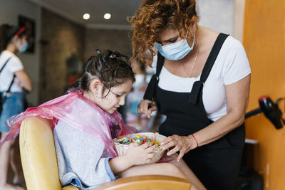 Hairdresser and girl searching in basket with hair clips at barber shop during coronavirus