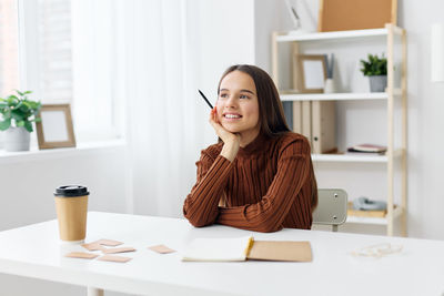 Young woman using mobile phone while sitting on table