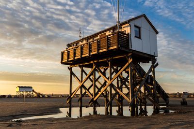 Lifeguard hut at beach against cloudy sky during sunset