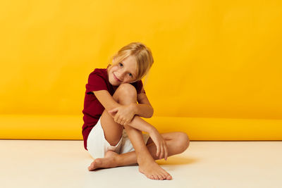 Portrait of cute girl sitting against yellow background