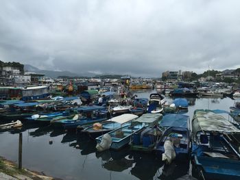 Boats moored at harbor against cloudy sky