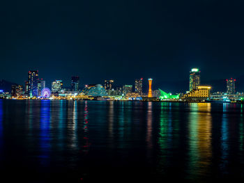 Illuminated city by sea against sky at night