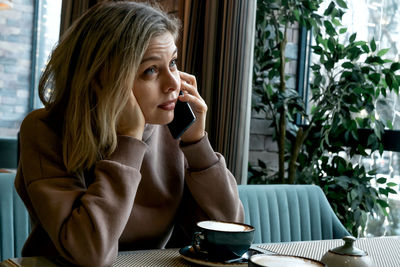 Caucasian middle-aged blonde woman sits in a cafe, drinks coffee and talks on a mobile phone