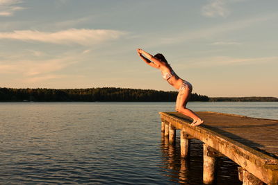 Side view of woman jumping in lake against sky during sunset