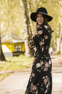 Portrait of smiling young woman wearing hat standing in park